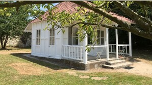 A small white building with a red roof, a porch, and a tree in the foreground. - The Grand Sambam (Fourdrain)