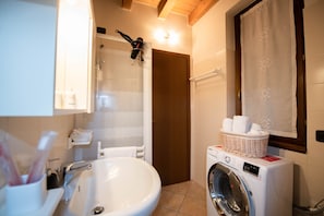 A bathroom with a sink, mirror, hanging hairdryer, and a washing machine with a basket of towels.