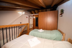 A bedroom with two beds, wooden beams, a staircase, and a small shelf with plants.