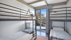Un dormitorio con literas, una puerta corrediza de vidrio a un balcón y vistas a árboles y cielo.