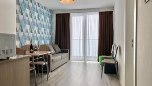 A modern living room with a sofa, a dining table with chairs, a TV, and a large window with curtains. - 2-room apartment NFT 452 New Gudauri (Gudauri)