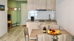 A compact kitchen with wooden cabinets, a sink, and a dining area with a table set for two. - 2-room apartment NFT 452 New Gudauri (Gudauri)
