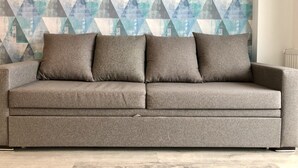 A grey sofa with three cushions against a geometric-patterned wall. - 2-room apartment NFT 452 New Gudauri (Gudauri)