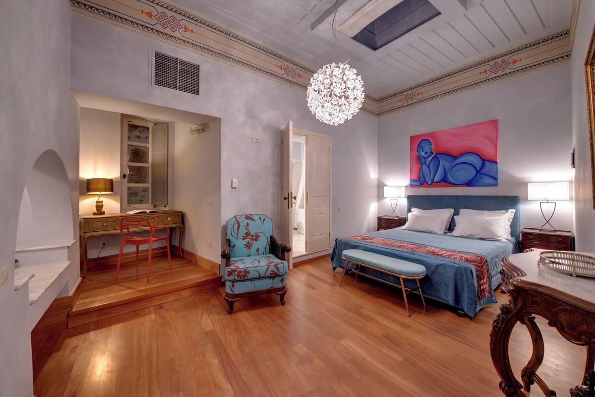 Ein Schlafzimmer mit Bett, Schreibtisch, Stuhl und einem großen Gemälde an der Wand.