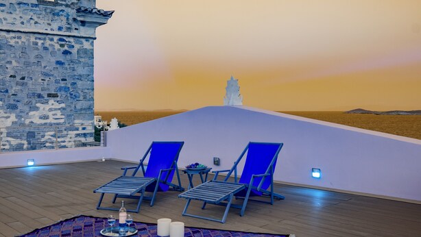 Una terraza en la azotea con dos sillones azules, una mesita con bebidas y un muro decorativo.