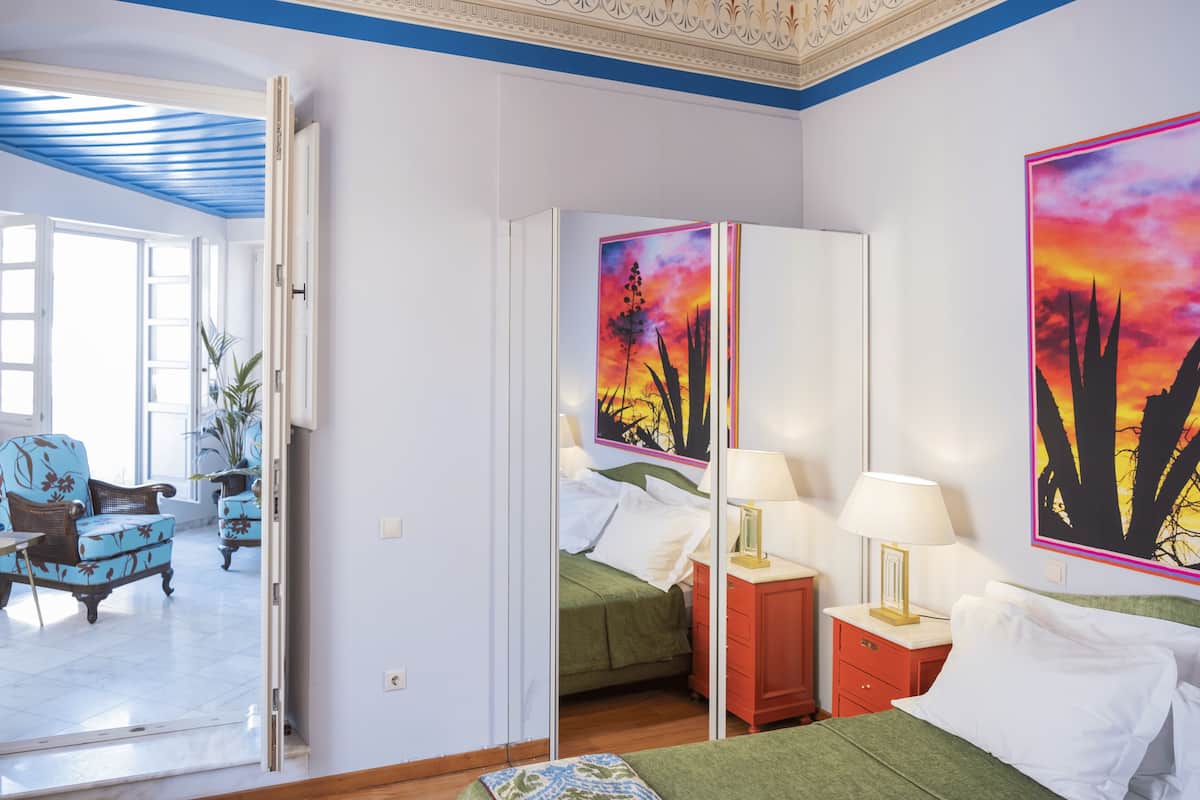 Ein Hotelzimmer mit Bett, Nachttischen, einem Spiegel und Blick auf den angrenzenden Wohnbereich.