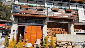 Una moderna cabaña con fachada de madera, un balcón con barandillas de madera y una pila de leña afuera.