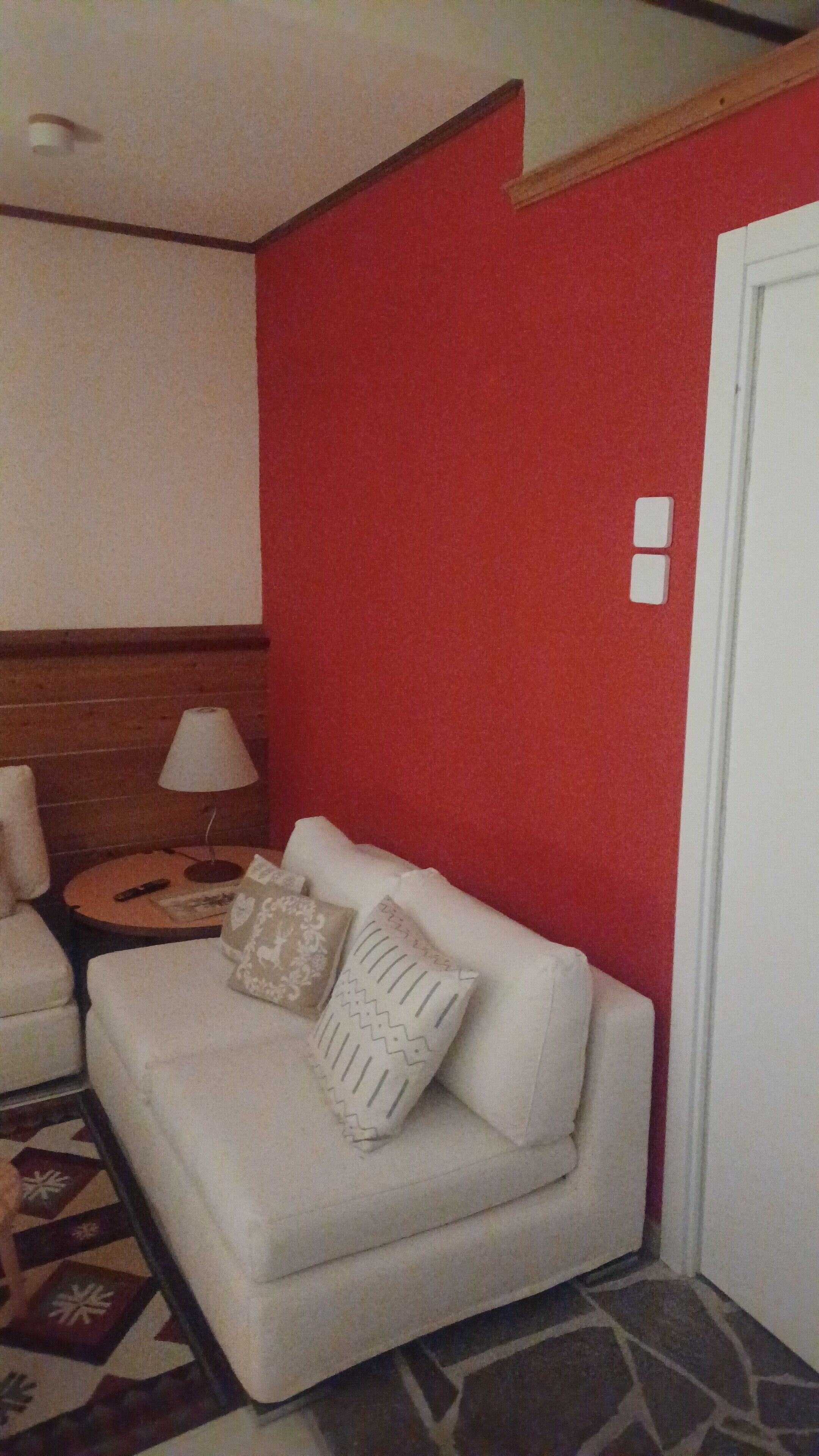 A white sofa with patterned cushions, a small round table with a lamp, and a red wall.