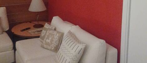 A white sofa with patterned cushions, a small round table with a lamp, and a red wall.
