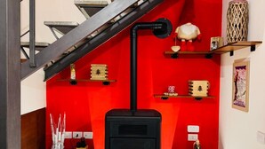Un interior moderno con un horno a leña negro, una pared de acento roja, una escalera y un suelo de piedra.