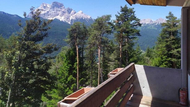 Una terraza de madera con vistas a montañas nevadas y un bosque denso.