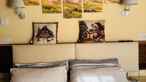 Habitación de hotel con una cama, dos lámparas fijadas a la pared, un cabecero y tres cuadros con paisajes sobre la cama.