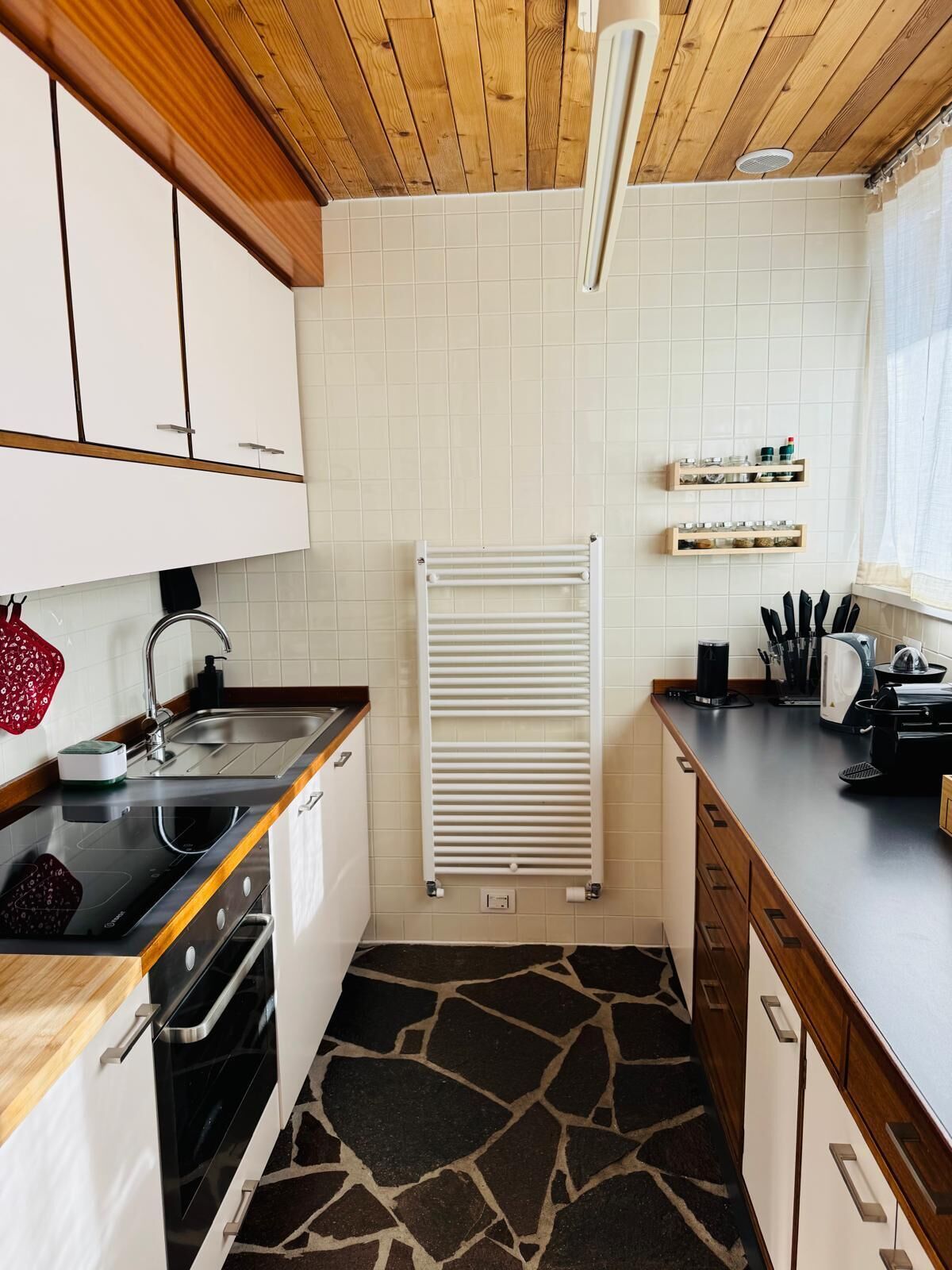 A compact kitchen with white cabinets, a black countertop, a stove, and a tiled backsplash.