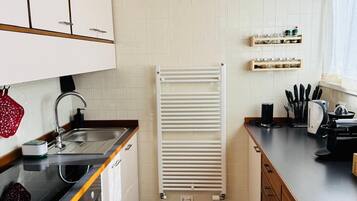 A compact kitchen with white cabinets, a black countertop, a stove, and a tiled backsplash.