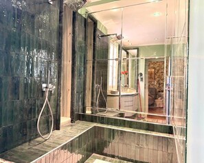 A modern bathroom with a glass shower enclosure, a visible sink, and a mirror reflecting the room.