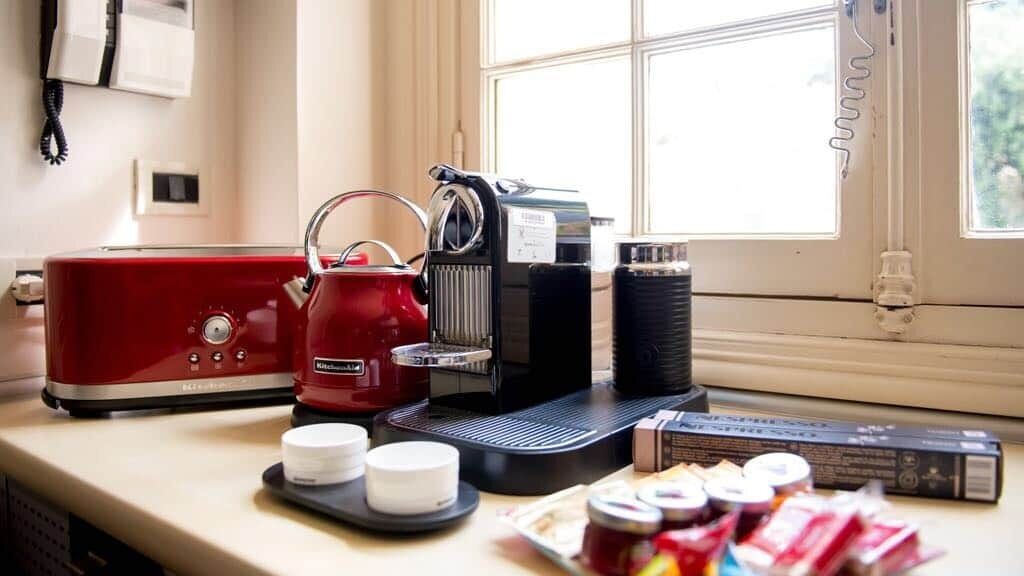 A kitchen counter with a red toaster, a coffee maker, and a coffee pot. There are jars of condiments and a box of tea bags.