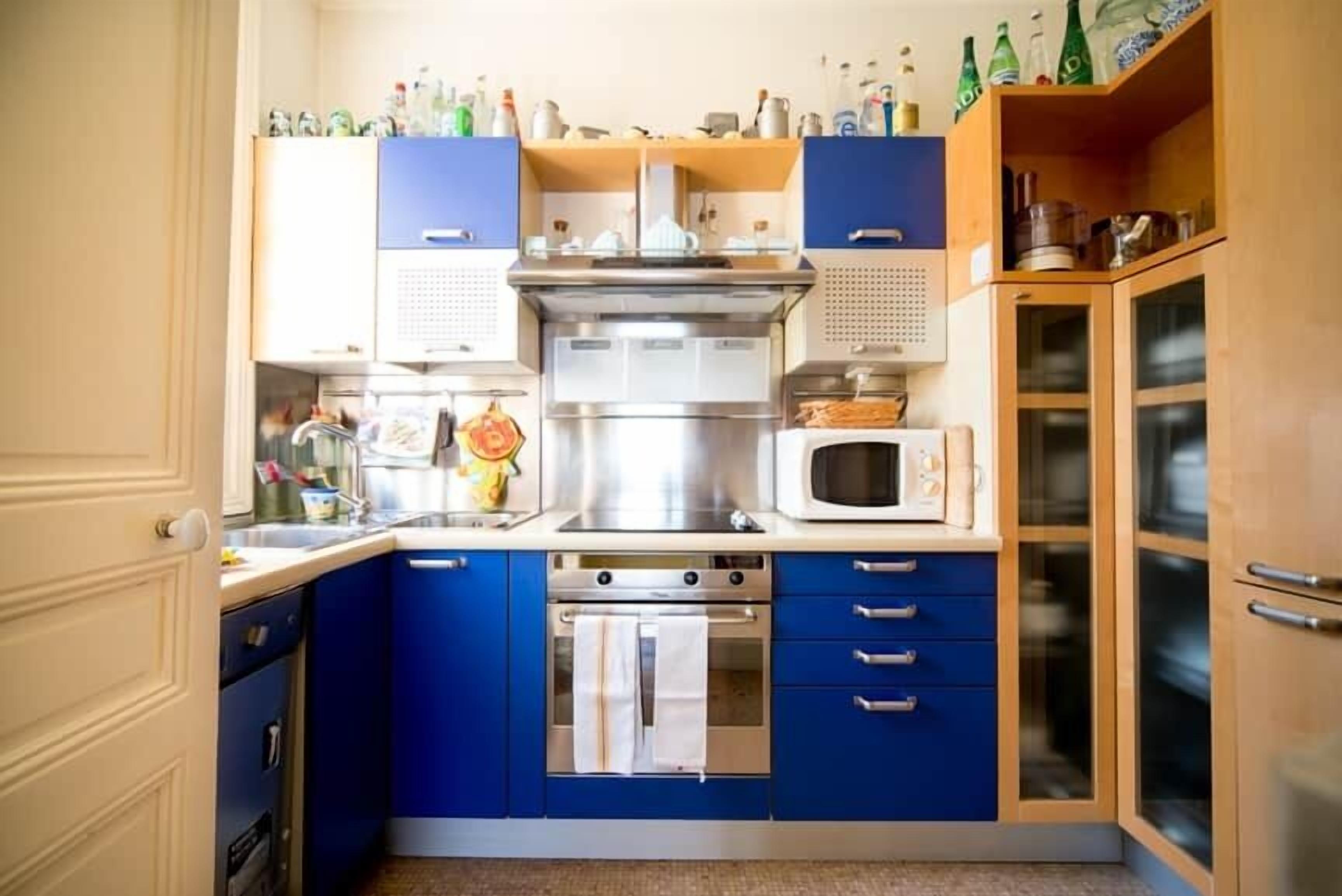 A kitchen with blue cabinets, a stainless steel range, a microwave, and a dish rack.