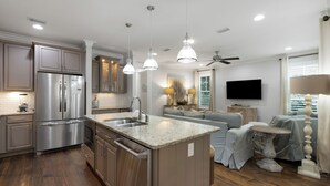 A modern kitchen with stainless steel appliances, a granite countertop island, and a dining area with a round table. - Watersound - Golf Cart - Pet Friendly - Bikes (Watersound)