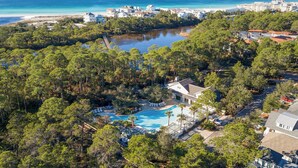 An aerial view of a resort with a swimming pool surrounded by dense trees, a beach, and ocean views. - Watersound - Golf Cart - Pet Friendly - Bikes (Watersound)