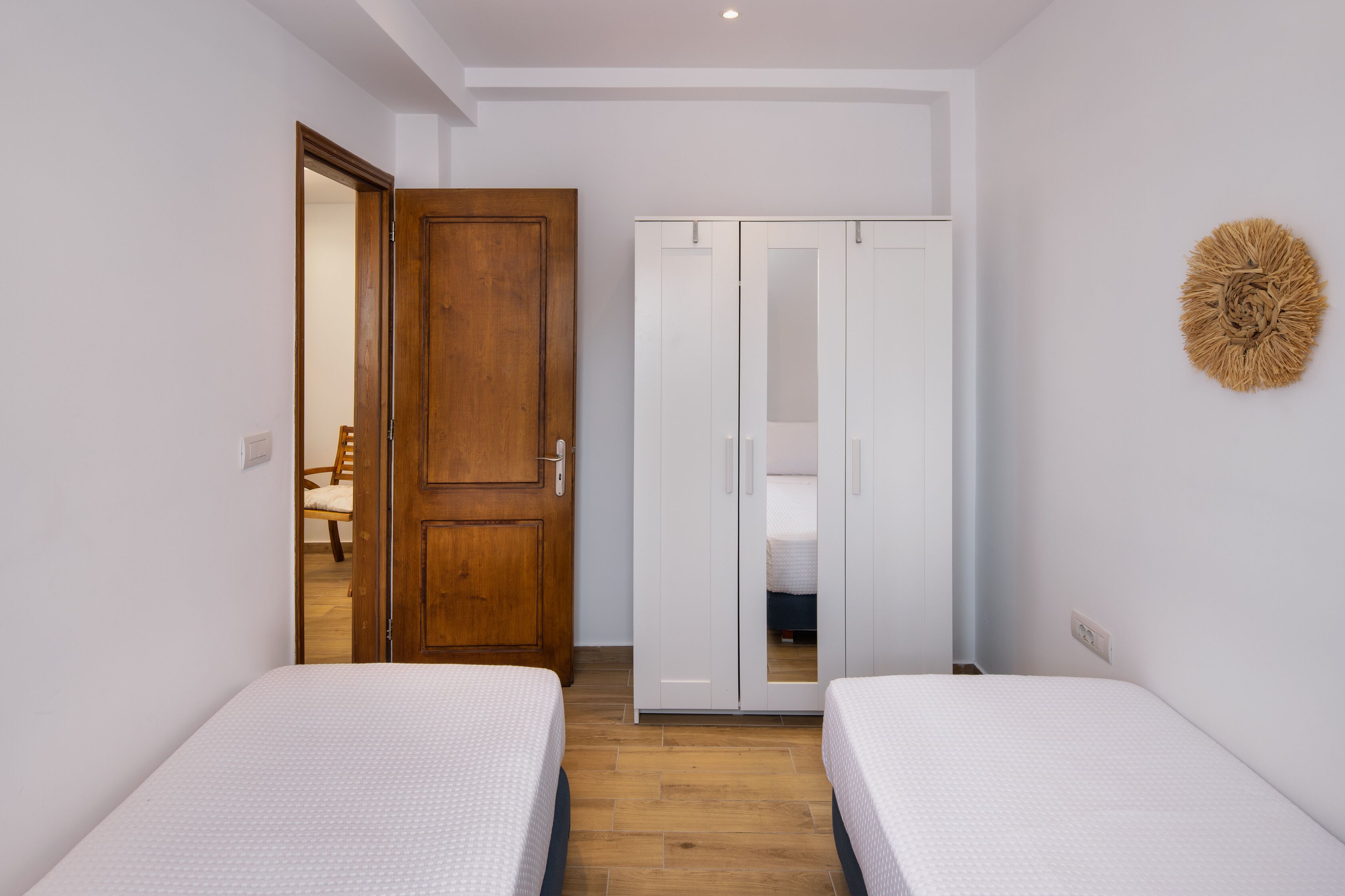 Une chambre avec deux lits simples, une armoire en bois et une armoire blanche.