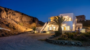 A modern house with a staircase leading to the upper floor, surrounded by a gravel driveway and a palm tree. - Pure Seaside Calm, Far from Santorini’s Crowds (Thira)