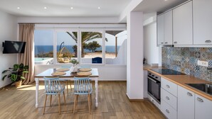 A modern kitchen with a view of the sea, a dining area with a table and chairs, and a TV mounted on the wall. - Pure Seaside Calm, Far from Santorini’s Crowds (Thira)