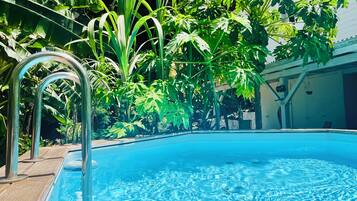 A swimming pool with clear water, surrounded by lush greenery and a wooden deck.