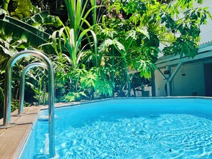 A swimming pool with clear water, surrounded by lush greenery and a wooden deck.