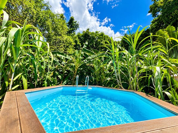 A rectangular pool with a wooden deck, surrounded by lush greenery and trees. - Les Vanilles Vacation Home in Lush Tropical Surroundings, Pool 800 m from the Beach (Deshaies)