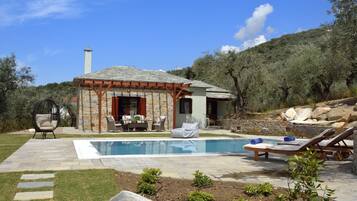 Una casa de piedra con piscina, mobiliario exterior y jardín.