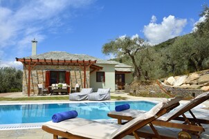 Un área junto a la piscina con sillones de descanso y una pérgola.
