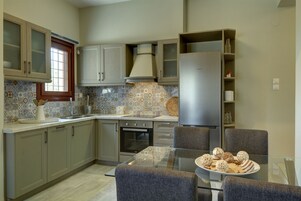 Una cocina moderna con una mesa de comedor de vidrio, armarios grises y un refrigerador de acero inoxidable.