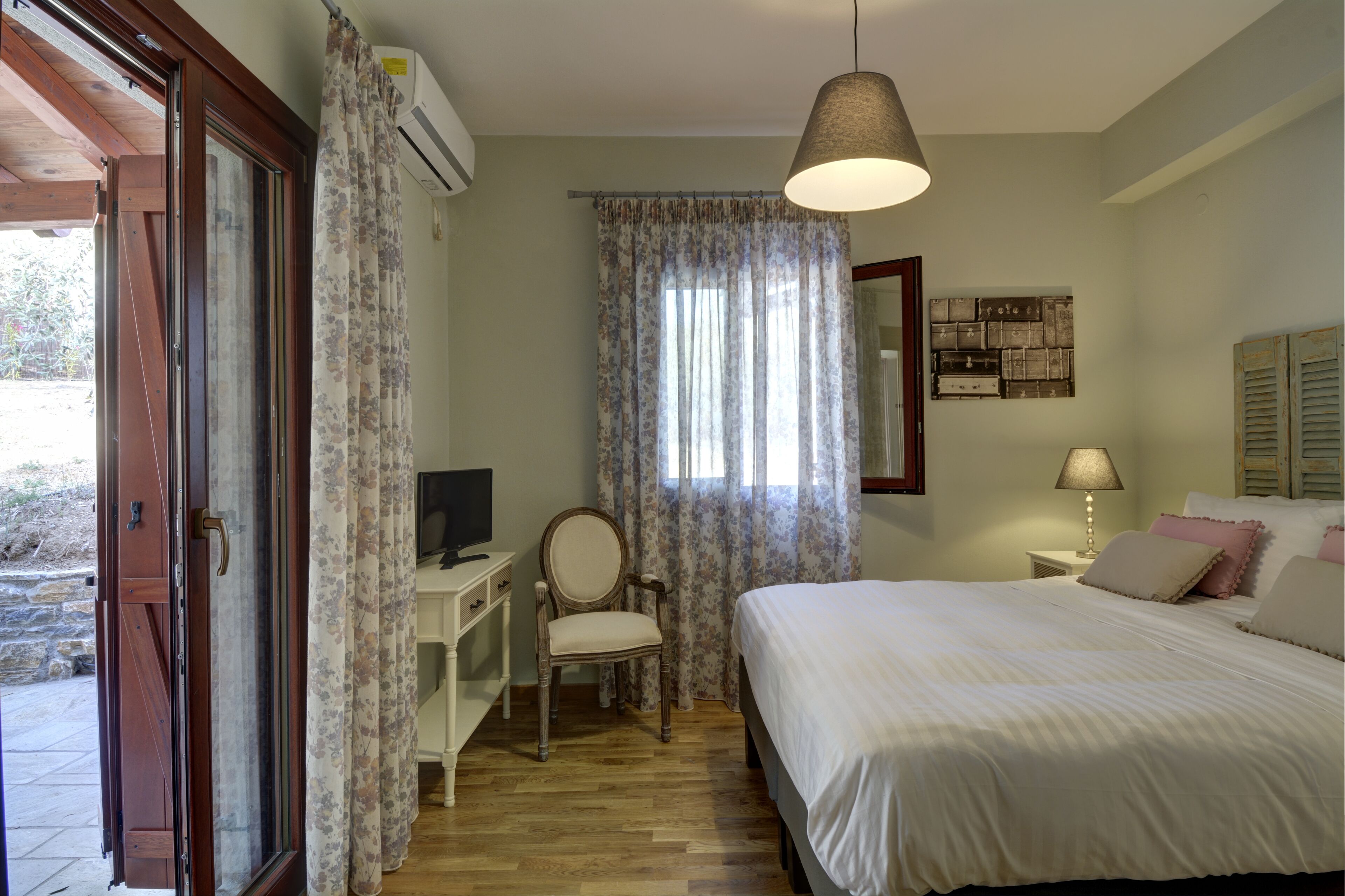 A bedroom with a bed, a chair, a desk, a television, and a window with curtains.