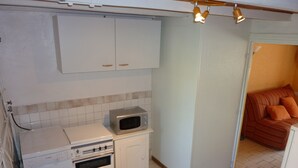 A compact kitchen with a Bosch washing machine, a microwave, and a small oven. There is a dining table with chairs and a sofa in the adjacent living area. - HOUSE IN A SMALL CHARMING VILLAGE: GOOD PRICE-QUALITY RATIO (AUZELLES)
