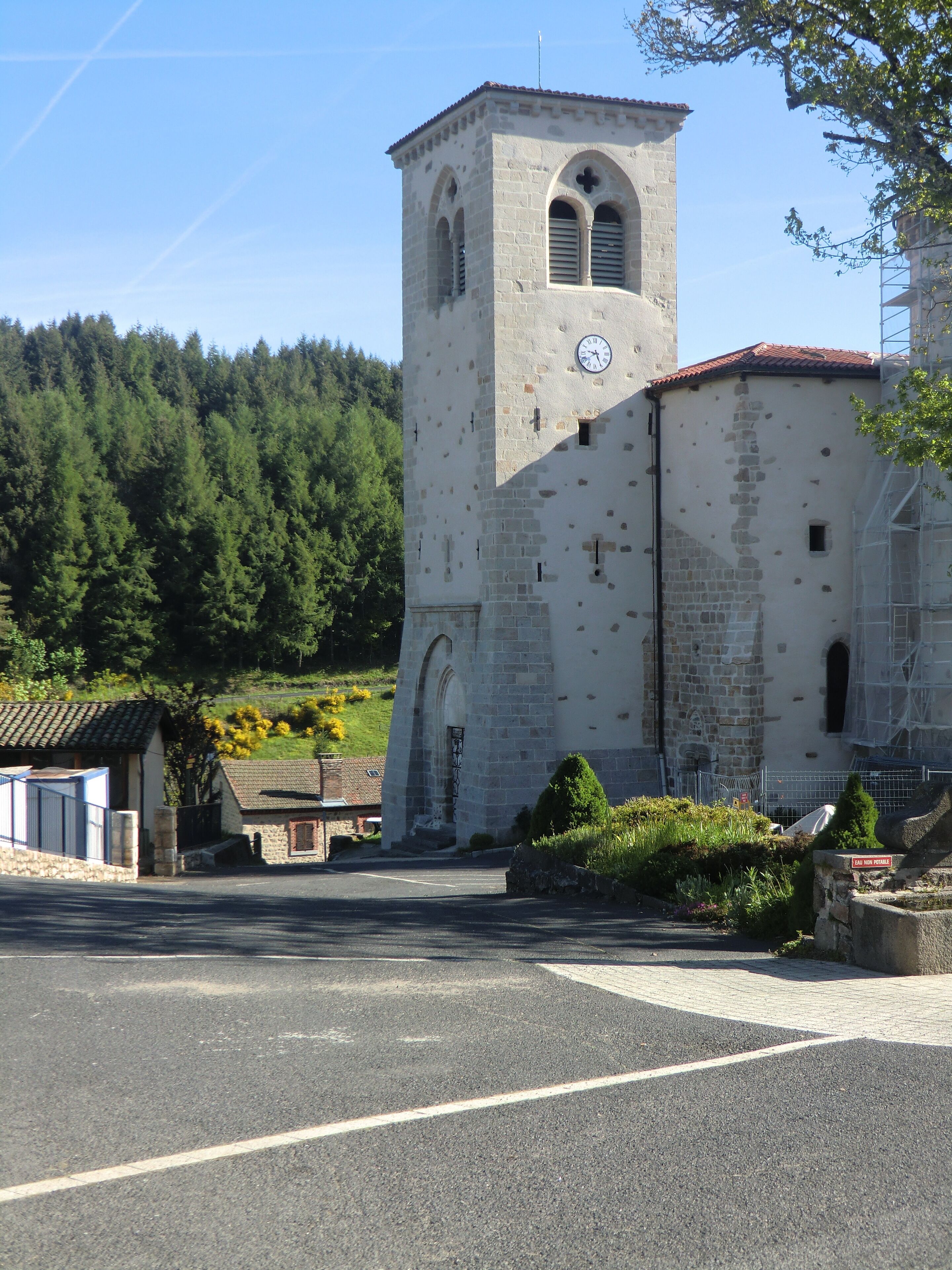 Un edificio de piedra histórico con una torre de reloj, una entrada con portones y un camino pavimentado al frente.