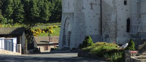 Un edificio de piedra histórico con una torre de reloj, una entrada con portones y un camino pavimentado al frente.