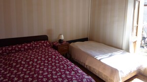 A bedroom with a large bed, a smaller bed, a nightstand with a lamp, and a window with curtains. - HOUSE IN A SMALL CHARMING VILLAGE: GOOD PRICE-QUALITY RATIO (AUZELLES)