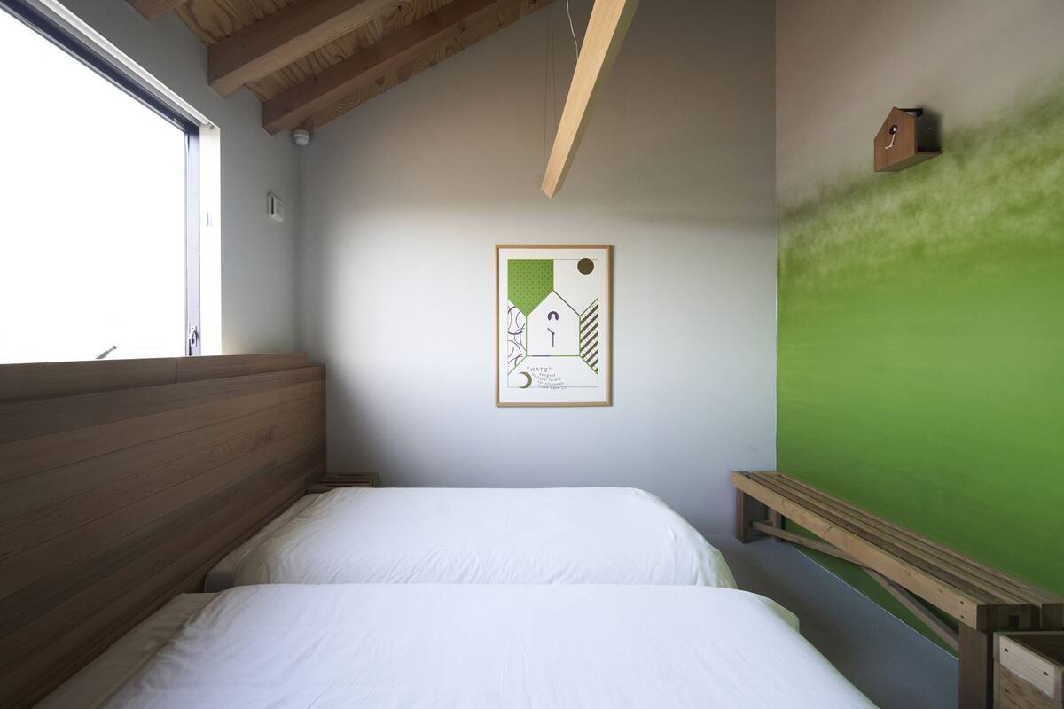 Quarto com duas camas, cabeceira de madeira, parede verde e quadro pendurado na parede.