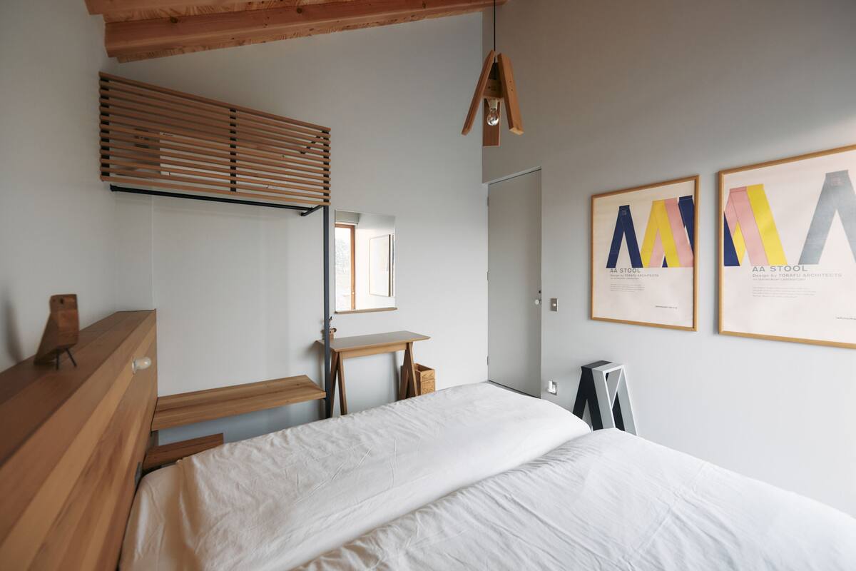 Um quarto com estrutura de cama de madeira, uma escrivaninha, uma janela com persianas e dois certificados emoldurados na parede.