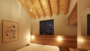 A bedroom with a wooden ceiling, a large window with a night view, and a framed artwork on the wall.