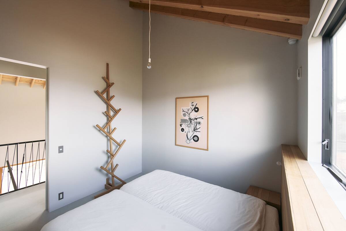 Quarto com cama, escada de madeira, quadro emoldurado e janela.