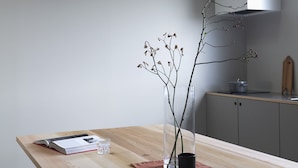 A wooden dining table with a vase of branches and a book.