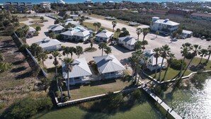 An aerial view of a coastal resort with multiple bungalow-style buildings, a marina, and a boardwalk leading to the beach. - Cottage with Boat Dockage, Steps to Private Beach Access! (St. Augustine)