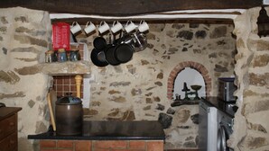 Una cocina rústica con paredes de piedra, ollas colgantes, un horno de ladrillo y una lavadora.