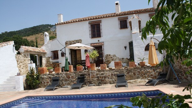 Una villa blanca con piscina, muros de piedra y mobiliario de exterior.