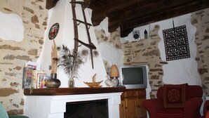 Una habitación rústica con paredes de piedra vista, techo de madera, chimenea, televisor y un sillón rojo.