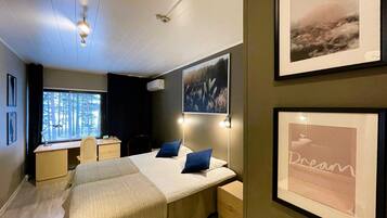 A hotel room with a bed, bedside tables, a desk, and a window with a view of trees.