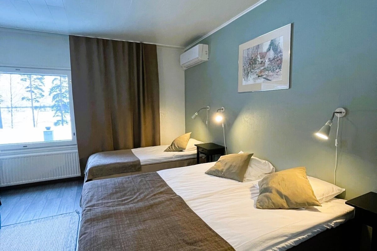 A hotel room with two beds, a window with curtains, a wall-mounted air conditioner, and a framed picture.