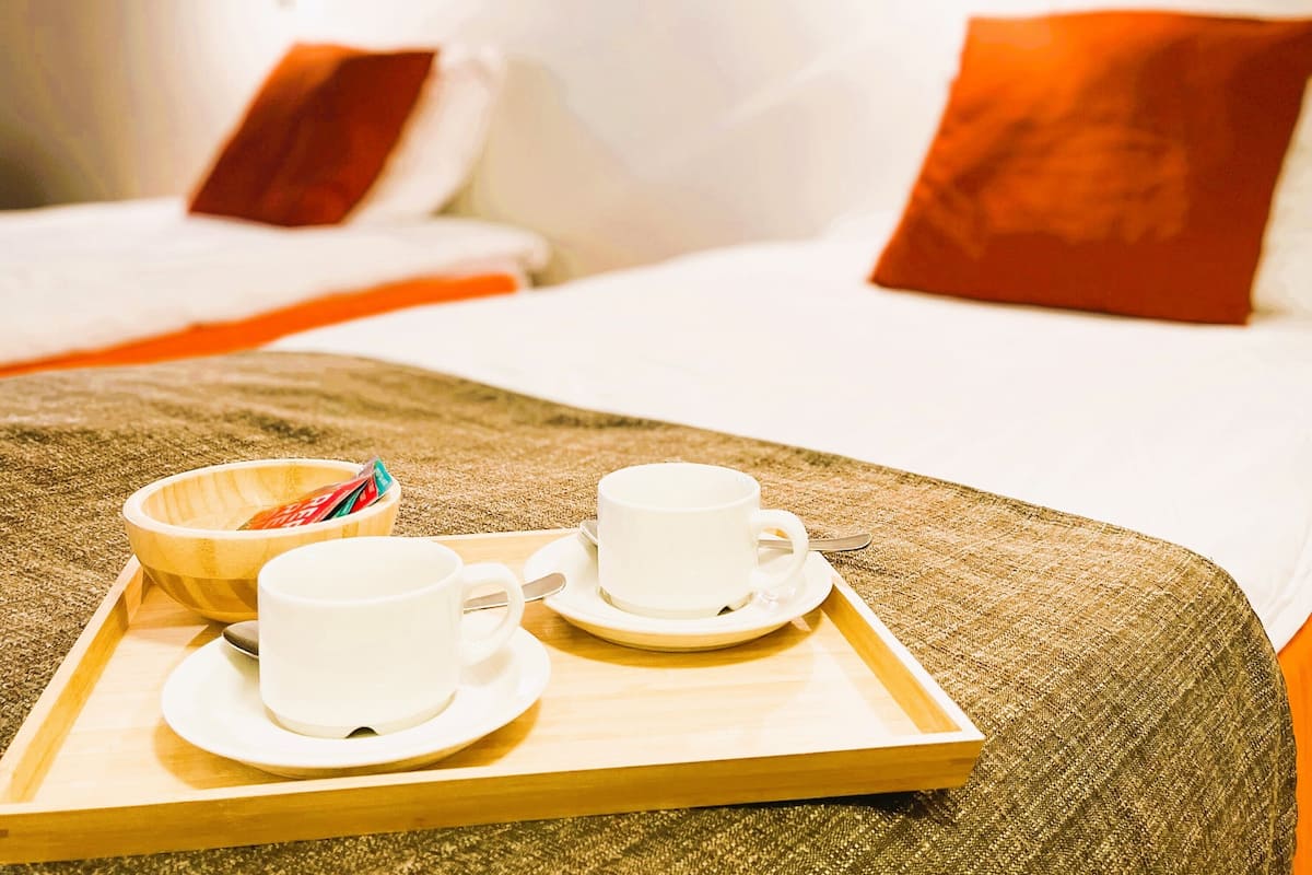 A hotel room with two beds, a painting on the wall, and a tray with cups and a bowl.