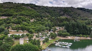 An aerial view of a lakeside property with multiple cabins, a dock with boats, and a surrounding forested area. - Camping Lac de Villefort (Pourcharesses)